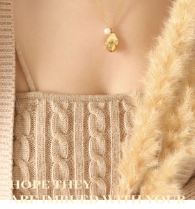 Macro shot of 18K gold plated necklace with pearl and hammered pendant on a beige sweater