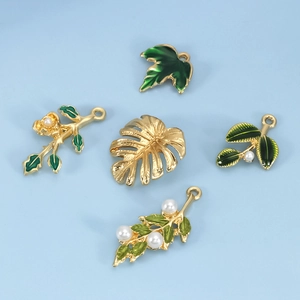 Detail of five gold-plated leaf charms with green enamel and white pearls for DIY jewelry