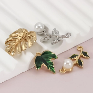 Detailed macro view of tropical leaf enamel charms and pearls on a white display stand