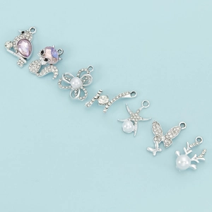Detalle de dijes plateados con pedrería, perlas y estrellas para hacer joyas artesanales