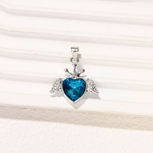 Detalle de un colgante de corazón azul oscuro con alas plateadas y corona fina