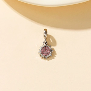 Detail of silver sun charm featuring a vibrant pink crystal inlay and polished bale