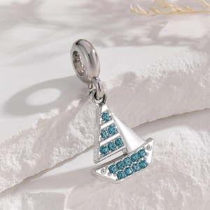 Macro shot of silver sailboat pendant charm featuring sparkling blue zircon gemstones