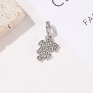 Sparkling silver puzzle piece pendant with pavé crystals on textured stone background