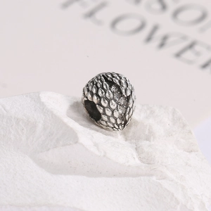 Macro detail of silver dragon egg charm with scale texture and small zircon inlay