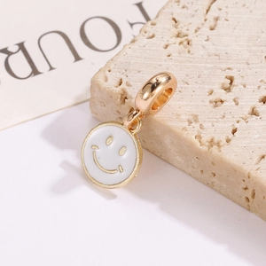 Macro view of a gold-edged white enamel smiley face pendant resting on a textured stone