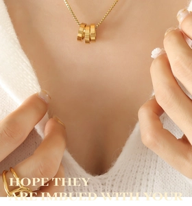 Detail of double-layer gold necklace with three-ring pendant on white knitwear background