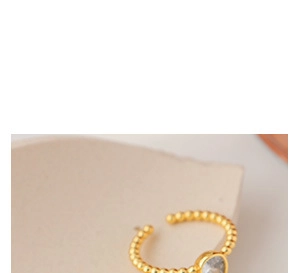 Détail d'une bague ouverte dorée perlée avec une pierre précieuse ronde translucide
