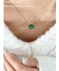Gros plan d'un collier doré avec pendentif malachite rotatif sur un pull blanc tricoté