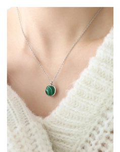 Détail d'un pendentif boule en malachite verte sur une chaîne en acier argenté sur un pull