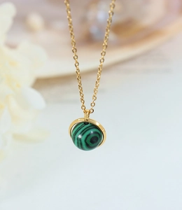 Vue macro du pendentif sphère en malachite rotative sur une chaîne en acier titane doré