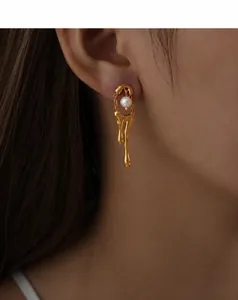 Close-up of molten metal gold earrings with white pearl detail on a model