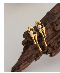 Detail of gold water-drop earrings with white pearls on dark textured wood background