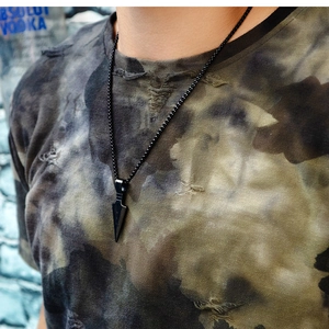 Detail of matte black arrowhead pendant necklace on a male model with street style camo tee
