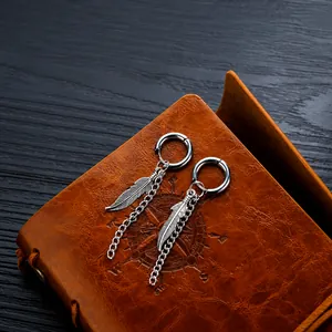 Detalle de pendiente con colgante de pluma y cadena sobre un cuaderno de cuero