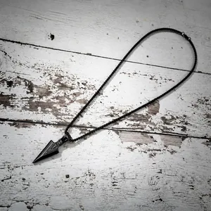 Macro detail of a black matte stainless steel arrowhead pendant on a vintage wood background