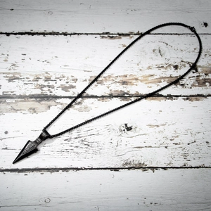 Men's black stainless steel spearhead pendant necklace on a white wooden background