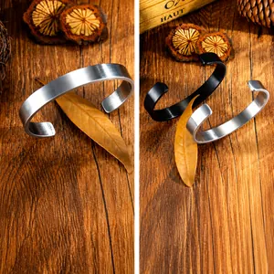 Detalle de pulseras de puño en C plateadas y negras con textura de acero inoxidable cepillado