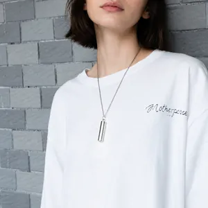 Polished stainless steel cylinder urn necklace for pet ashes worn against a gray wall