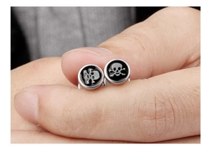 Makroaufnahme von Punk-Totenkopf-Ohrsteckern aus Edelstahl zwischen Fingern zur Größe
