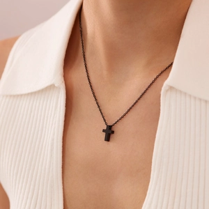 Close-up of a minimalist matte black cross pendant necklace worn with a white sweater