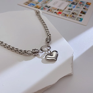 Detalle de un collar con colgante de corazón plateado sobre una superficie de piedra blanca