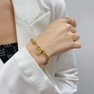 Detalle de pulsera con colgante de corazón dorado y anillo minimalista en mano de modelo