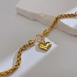 Detalle macro de pulsera de cadena dorada con colgante de corazón pulido y cuentas roscadas