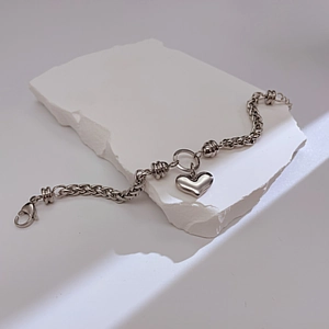Detalle de una pulsera de cadena gruesa con dije de corazón sobre piedra blanca
