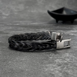 Macro view of woven leather bracelet featuring a matte metal clasp on stone background