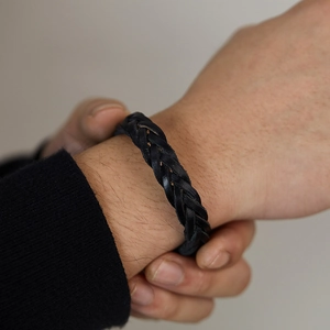 Close-up detail of hand-woven black leather bracelet showing premium grain texture