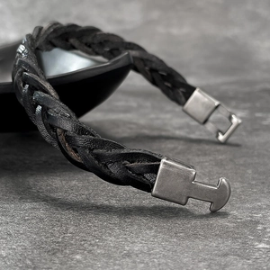 Macro shot of a black braided leather bracelet featuring a vintage brushed metal T-bar clasp