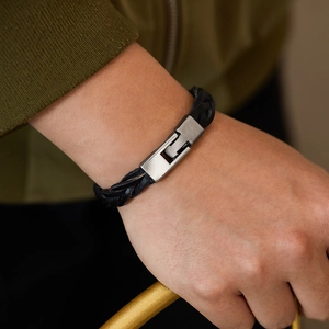 Close-up of a hand-woven black leather bracelet with a matte silver metal clasp