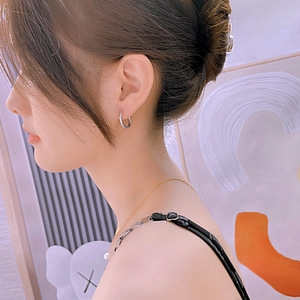 Close-up of a silver geometric stainless steel hoop earring worn by a model