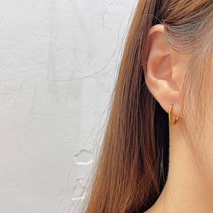 Close-up of a model wearing a polished gold oval hoop earring made of titanium steel