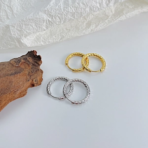 Detail view of gold and silver hammered texture hoop earrings on minimalist background