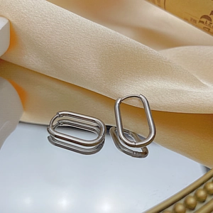 Macro view of silver oval hoop earrings on reflective mirror with silk background
