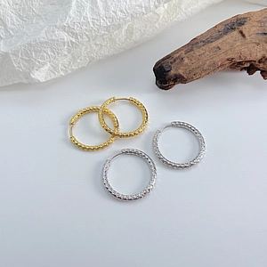 Detail view of gold and silver geometric hoop earrings with textured scale pattern on wood