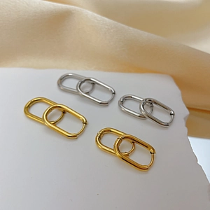 Polished titanium steel oval hoop earrings in gold and silver on elegant fabric
