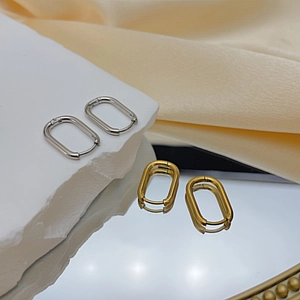 Macro detail of oval gold and silver steel hoop earrings on elegant silk background