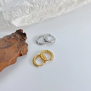 Detail view of gold and silver hammered titanium steel hoop earrings on a minimalist wooden base