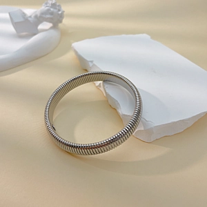 Polished silver titanium steel bangle with spiral texture shown on a white stone slab