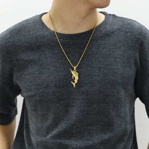 Close-up of golden marlin fish pendant with box chain on a grey textured sweater