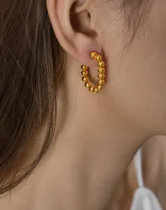 Primer plano de pendientes de aro dorados con cuentas en modelo de diseño minimalista