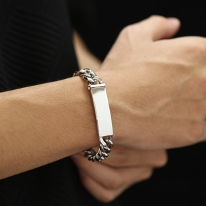 Κοντινό πλάνο ασημένιου βραχιολιού cuban link με γυαλισμένη πλάκα χάραξης στον καρπό