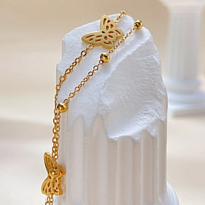 Detailansicht eines goldenen Schmetterlings-Fußkettchens mit Perlen auf Marmorsäule