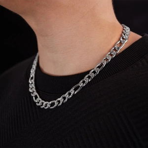 Gros plan d'une grosse chaîne Figaro en argent portée par un mannequin sur un pull noir texturé