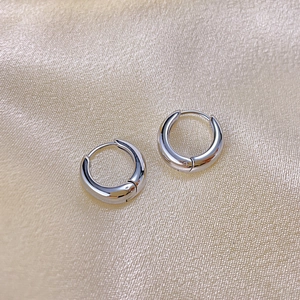 Gros plan de boucles d'oreilles créoles en acier poli sur fond de soie élégant