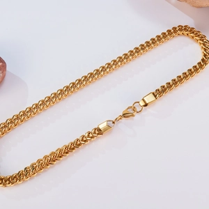 Close-up of thick gold Cuban link necklace with lobster clasp on natural stone base