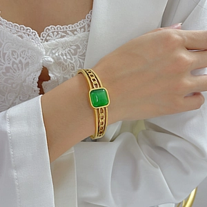 Macro detail of vintage gold bangle featuring square green gemstone and chain textures
